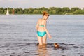 Mature caucasian woman plays ball in water with dog of Dachshund breed. Summertime theme with pet swim in river. Hot weather in Royalty Free Stock Photo