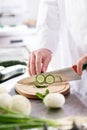 Midsection of mature chef cutting cucumber on board in restaurant kitchen