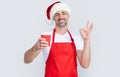 mature christmas man in red santa hat and apron hold coffee cup. ok Royalty Free Stock Photo