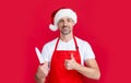 mature christmas man in red santa hat and apron hold kitchen knife. thumb up Royalty Free Stock Photo