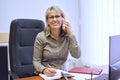 Mature confident businesswoman at workplace talking on mobile phone, writing in business notebook Royalty Free Stock Photo