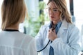 Mature confident female doctor examining with stethoscope to young patient in the medical consultation Royalty Free Stock Photo