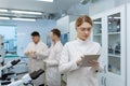 Mature confident and serious thinking woman in white medical coat working with tablet computer, team of scientists