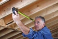 Mature construction worker measuring distance between rafter beams.