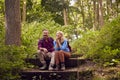 Mature Couple In Countryside Hiking Along Path Through Forest Sit And Take A Break Together