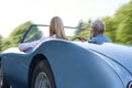 Rear View Of Mature Couple Enjoying Road Trip In Classic Open Top Sports Car Together