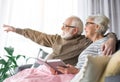 Senior husband ponting at window while sitting on couch