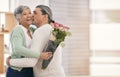 Mature couple, flowers and kiss at home for anniversary, birthday or valentines celebration. Surprise, love and roses Royalty Free Stock Photo