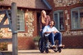 Mature Couple With Man Sitting In Wheelchair Being Pushed By Woman Outside Home Royalty Free Stock Photo