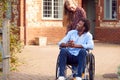 Mature Couple With Man Sitting In Wheelchair Being Pushed By Woman Outside Home Royalty Free Stock Photo