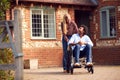 Mature Couple With Man Sitting In Wheelchair Being Pushed By Woman Outside Home Royalty Free Stock Photo