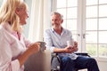 Mature Couple With Man In Wheelchair Sitting In Lounge At Home Talking Together Royalty Free Stock Photo