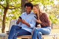 Mature Couple Meeting In Outdoor Park Sitting On Bench Looking At Mobile Phones Together Royalty Free Stock Photo