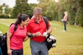 Mature Couple Playing Round Of Golf Carrying Golf Bags And Marking Scorecard