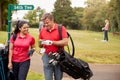 Mature Couple Playing Round Of Golf Carrying Golf Bags And Marking Scorecard