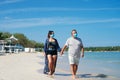 Couple with protective mask holding hands and strolling on the beach Royalty Free Stock Photo