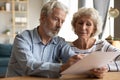 Mature couple read medical insurance terms seated at table indoors