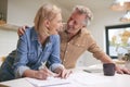 Mature Couple Reviewing And Signing Domestic Finances And Investment Paperwork In Kitchen At Home Royalty Free Stock Photo