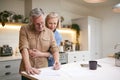 Mature Couple Reviewing And Signing Domestic Finances And Investment Paperwork In Kitchen At Home Royalty Free Stock Photo