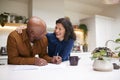 Mature Couple Reviewing And Signing Domestic Finances And Investment Paperwork In Kitchen At Home Royalty Free Stock Photo