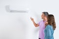 Couple Adjusting Temperature Of Air Conditioner Royalty Free Stock Photo