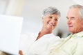 Mature couple using laptop at home. Smiling mature couple using laptop while sitting on couch. Royalty Free Stock Photo