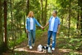 A mature couple is walking with a dog in a park. Man and woman in shirts and jeans. Stylish and modern grandparents Royalty Free Stock Photo