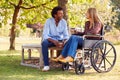 Mature Couple With Woman Sitting In Wheelchair Talking And Drinking Coffee In Park Together Royalty Free Stock Photo