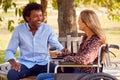 Mature Couple With Woman Sitting In Wheelchair Talking And Drinking Coffee In Park Together Royalty Free Stock Photo