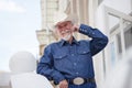 A mature cowboy in a hat, jeans and a denim shirt looks at the camera. On open air. Royalty Free Stock Photo