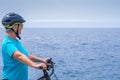Mature cyclist woman enjoying activity at sea with her electro bike. Standing looking at horizon over water
