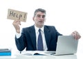 Mature desperate businessman suffering stress working at computer desk holding sign asking for help looking stressed overworked