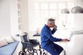 Mature Disabled Man In Wheelchair At Home Using Laptop On Kitchen Counter Royalty Free Stock Photo