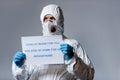 Mature doctor in hazmat suit holding placard with i stay at work for you, you stay at home for us lettering Royalty Free Stock Photo