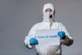 Mature doctor in hazmat suit holding placard with stay at home lettering Royalty Free Stock Photo