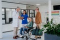 Mature doctor and his young colleague talking with his senior patients at hospital corridor.