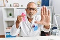 Mature doctor man holding pink cancer ribbon at the clinic with open hand doing stop sign with serious and confident expression, Royalty Free Stock Photo