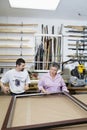 Mature employee measuring picture frame with senior owner in workshop