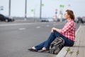 Mature woman hitchhiker sitting on roadside and waiting the car