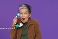 Mature excited, shocked grey haired woman chatting or gossiping on the phone holding retro telephone handset wearing Royalty Free Stock Photo