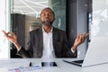 Mature experienced african american boss meditating inside office workplace sitting at desk, man with closed eyes Royalty Free Stock Photo