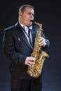 Mature Expressive Caucasian Saxophonist in Dark Suit Posing Against Seamless Black Background