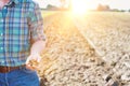 Mature farmer examining soil in field with yellow lens flare in background