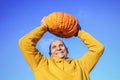 Mature farmer rising large yellow pumpkin over head standing against blue sky