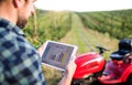 A mature farmer with tablet standing by mini tractor outdoors in orchard. Royalty Free Stock Photo