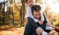 Mature father giving piggyback ride to small daughter on a walk in autumn forest. Royalty Free Stock Photo