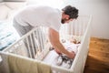 Father putting a sleeping toddler girl into cot at home.