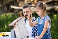 Father with a small daughter outside, painting wooden birdhouse. Royalty Free Stock Photo