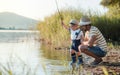 A mature father with a small toddler son outdoors fishing by a lake.