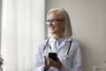 Mature female doctor standing at workplace with smartphone Royalty Free Stock Photo